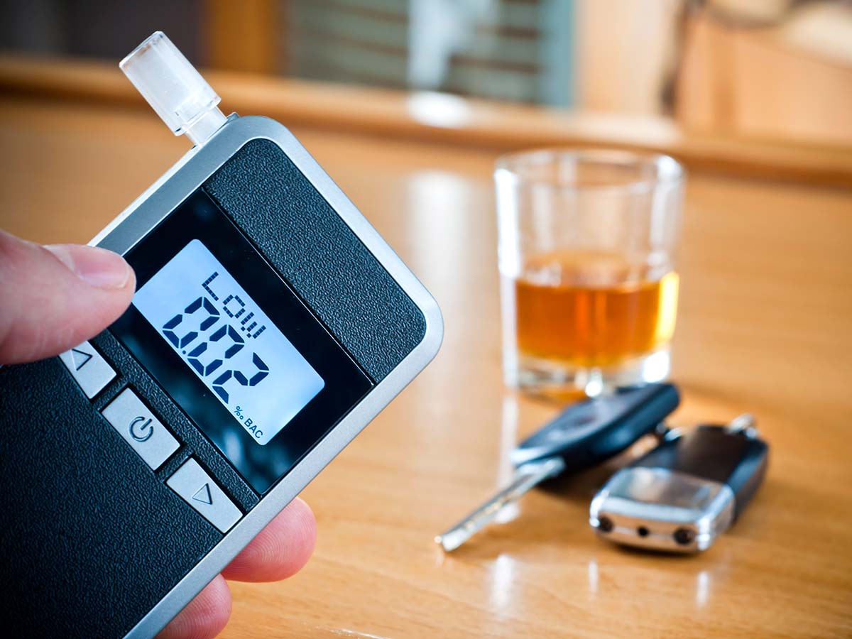 прибор для измерения степени опьянения на фоне стакана с алкоголем