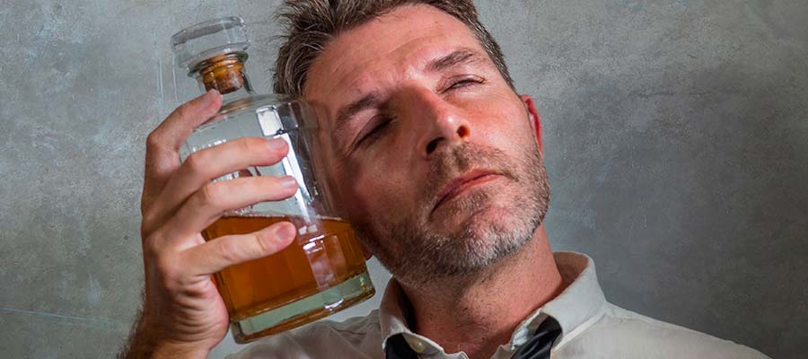пьяный мужчина закрыл глаза и приложил бутылку с алкоголем к голове